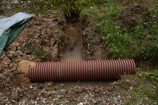 Corrugated plastic drainage pipe laid in ground ditch outdoors, drainage system installation, water management, groundwork development, spring season.