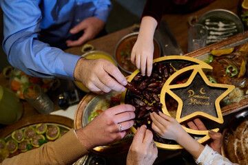 Fototapeta premium Ramadan Family Sharing Dates At Iftar Table Celebrating Ramadan Mubarak With Hands Reaching For Fruit