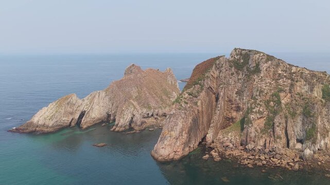 A stunning aerial shot captures the dramatic rocky cliffs and turquoise waters along the coastline near El Peine del Mar in Cudillero, Spain.