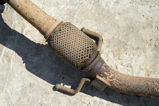 Worn and torn corrugated exhaust pipe of a car.