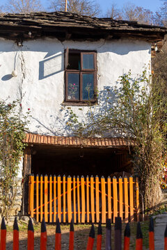 View of a traditional stone house with a white plaster facade, a wooden window, and an orange picket fence in the village of Gostusa, Stara planina, Pirot District, Serbia.