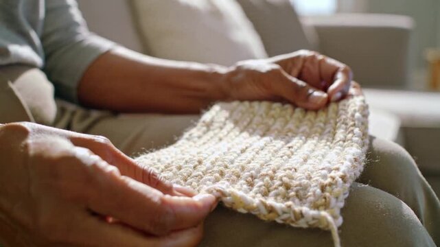 Hands resting, grey-top woman smoothing knit swatch on lap at home, inspecting stitch, tidying tail