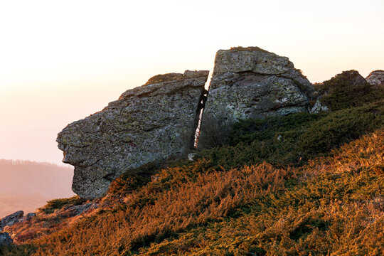 View of the split rock formation at Stara planina, surrounded by low shrubs on a hillside during the golden hour in Babin zub, Pirot District, Serbia.