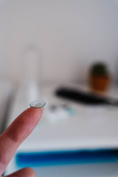 Orthokeratology night lens held on a fingertip with lens case and eye care supplies. Overnight corneal reshaping supports myopia control and daytime vision