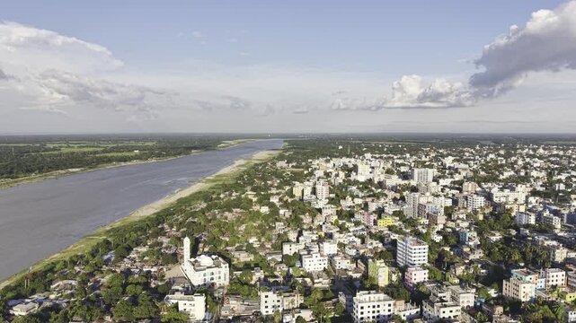 Drone footage overlooking the Gorai River and Kushtia city, with urban buildings, riverside greenery, open landscape, and a broad cloudy sky.