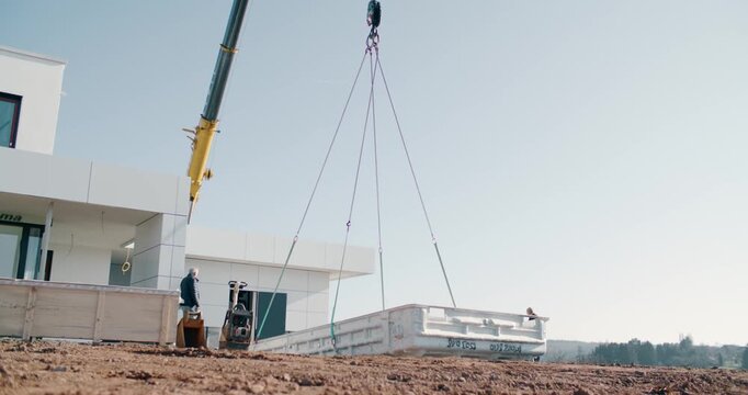 Crane lifts a concrete element beside a modern white building