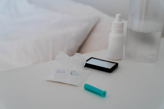 Orthokeratology night lens cases, contact lenses, applicator and solution bottle on a bedside table. Myopia treatment uses Ortho K therapy for overnight corneal reshaping and myopia control.