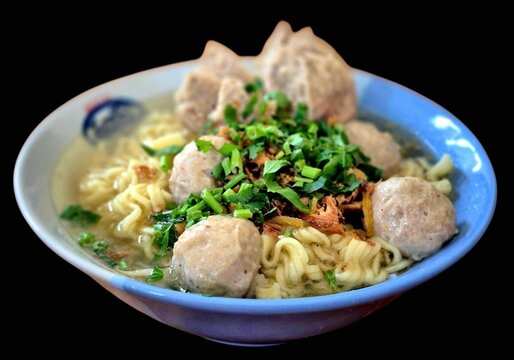 Indonesian meatballs bakso noodle soup topped with fresh celery and fried shallots isolated on black