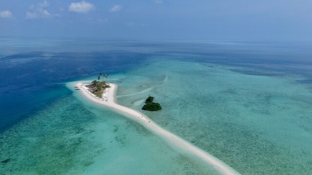 Aerial view of a narrow sandbar Manimbora island surrounded by turquoise and deep blue ocean waters in Indonesia.
