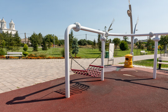Contemporary swing set in a landscaped park with benches, greenery, and open sky, ideal for recreation and outdoor activities.