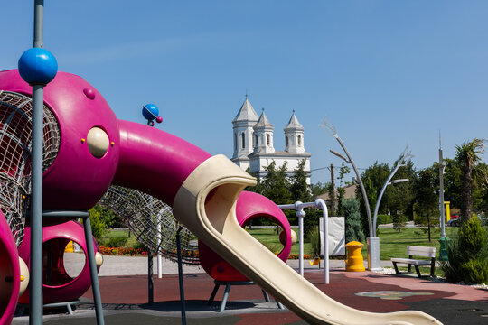 Colorful playground with slides and climbing structures in a park, featuring a historic white church in the background under a clear blue sky.