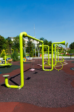 Vibrant green playground structure with swings and climbing elements on a sunny day, set on a safe rubber surface in a public park.