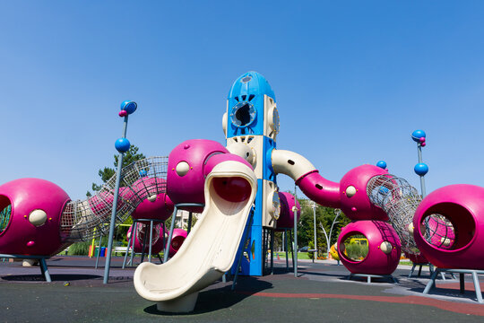 Colorful outdoor playground featuring a rocket-shaped slide, climbing tunnels, and vibrant play structures under a clear blue sky.