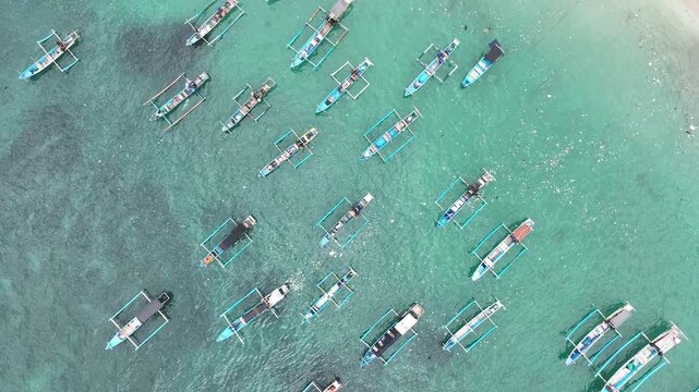 Aerial view of traditional outrigger boats floating on clear turquoise water in Lumajang, East Java, Indonesia.