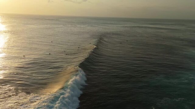 Cinematic aerial tracking of surfers in turquoise ocean water below Jaran Hill in Uluwatu Bali &ndash; Breathtaking bright daylight illuminating tropical sea surf lineup, commercial stock video 4k UHD asset