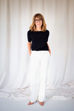Full lenght studio portrait of a blond haired mature woman in black shirt and white pants against isolated background