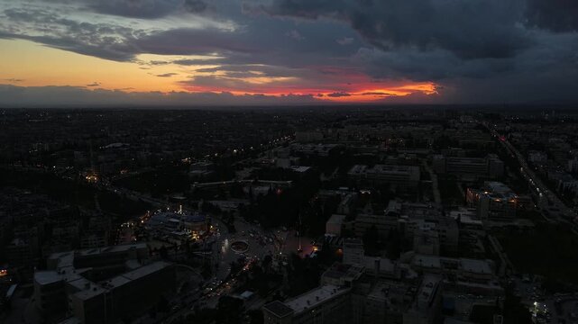 Aerial drone view of an urban landscape in Syria at sunset. City skyline and street lights during dusk. Middle Eastern city view under colorful evening clouds.