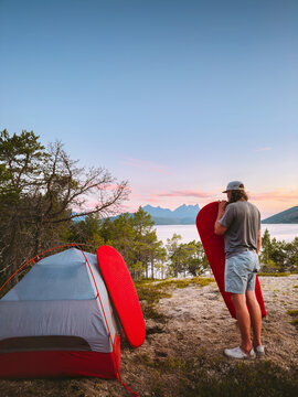Camping travel with tent in Norway - man inflates sleeping pad gear outdoors adventure healthy lifestyle summer active vacations trip, backpacker with climbing equipment in the forest enjoying view