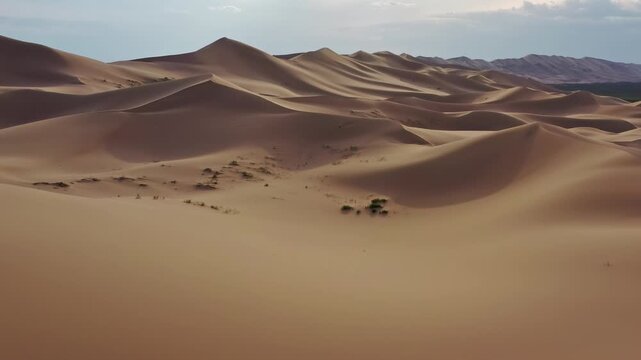 Aerial view of the vast Gobi Desert featuring rolling sand dunes under a bright sky in Mongolia.