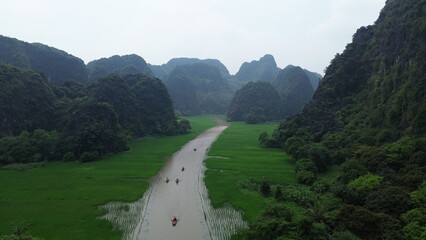 Drone shot of local rowers paddling with feet on Ngo Dong river through limestone valley, Ninh Binh, Vietnam © GeoWild