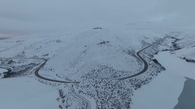 Aerial view of Lucky Peak Lake surrounded by snow-covered hills and a winding road in Ada County, Idaho, United States.
