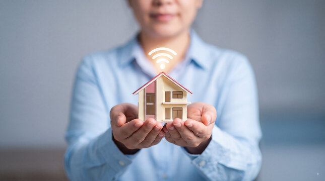 Woman holding miniature house with glowing wireless symbol, smart home automation, connected property technology and modern real estate concept