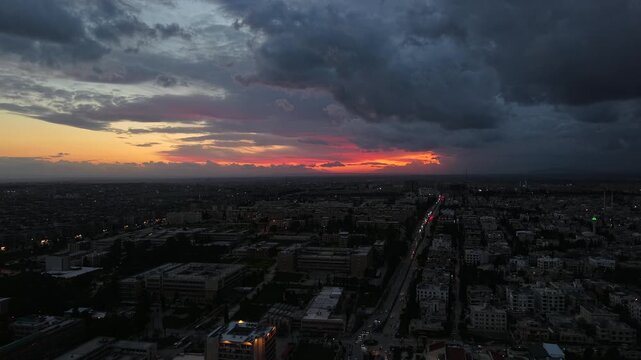 Aerial drone view of an urban landscape in Syria at sunset. City skyline and street lights during dusk. Middle Eastern city view under colorful evening clouds.