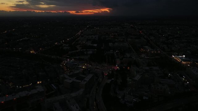 Aerial drone view of an urban landscape in Syria at sunset. City skyline and street lights during dusk. Middle Eastern city view under colorful evening clouds.