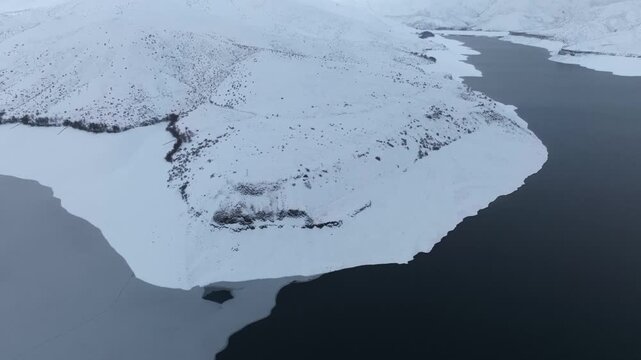 Aerial view of Lucky Peak Lake surrounded by snow-covered hills and icy water in Ada County, Idaho, United States.