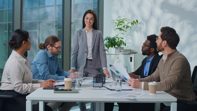 Caucasian businesswoman boss standing talking to successful business team coworkers at office meeting. Leader woman talk to managers colleagues presenting project corporate leading conference briefing