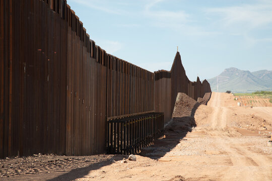 View of the steel border wall stretching across the desert landscape under a clear blue sky in Naco, Arizona, United States.