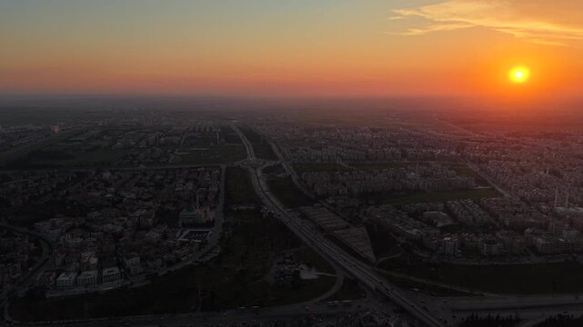 Aerial drone view of an urban landscape in Syria at sunrise. City skyline and residential neighborhoods bathed in morning light. Middle Eastern city view under a golden dawn sky. 