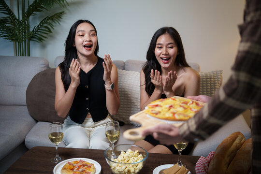 Young Asian women reacting happily as a friend serves pizza at a home party.