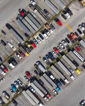 Aerial view of a large logistics parking lot filled with numerous semi-trucks, trailers, and passenger cars parked in orderly rows in Miami, Florida, United States.