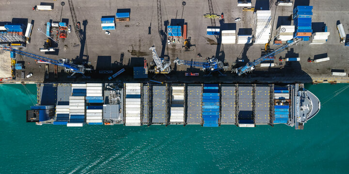 Aerial view of a large container ship docked at Port Miami, loaded with colorful shipping containers, surrounded by turquoise water and industrial infrastructure in Miami, Florida, United States.