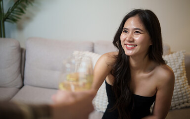 Naklejka premium Young Asian woman raising a wine glass during a cheerful home party.