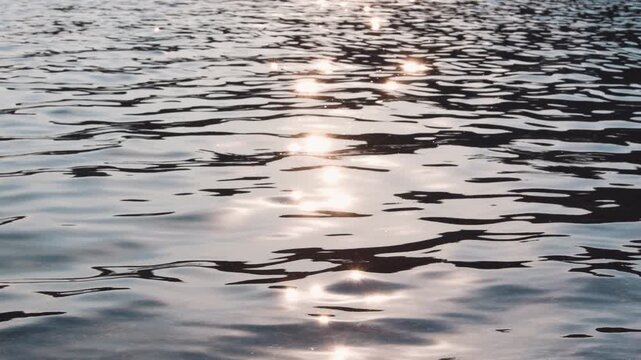 Sunlight glitters across rippling water, creating bright reflections and abstract patterns on calm surface. Soft waves and fluid textures evoke serenity nature relax peacefulness gentle motion