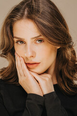 Fototapeta premium A close-up portrait of a thoughtful brunette woman with hand gently resting on her cheek. A soft beauty shot focusing on facial features and contemplative expression.