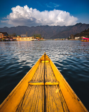 View of a traditional wooden shikara boat on the calm waters of Dal Lake with houseboats and mountains in the background in Srinagar, Jammu and Kashmir, India.