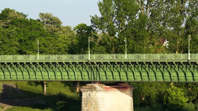 Daytime footage of the Pont Canal in Briare, France, featuring the iconic green metal canal bridge set against a backdrop of dense, vibrant green trees.