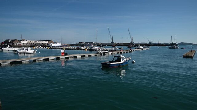 St Peter Port Harbour,Guernsey Channel Islands.Water level view of small boat bobbing in the harbour looking over pontoons to Cambridge Berth and docks with Jethou visible through harbour entrance