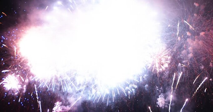 Fireworks explode above the ocean at night, filling the sky with colorful sparks, glowing smoke and dramatic reflections during a seaside celebration.