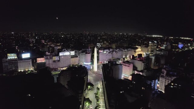 4K drone aerial view of the Obelisk and Corrientes Avenue in Buenos Aires, Argentina at night. The city&rsquo;s most iconic landmark surrounded by illuminated streets and vibrant urban life.