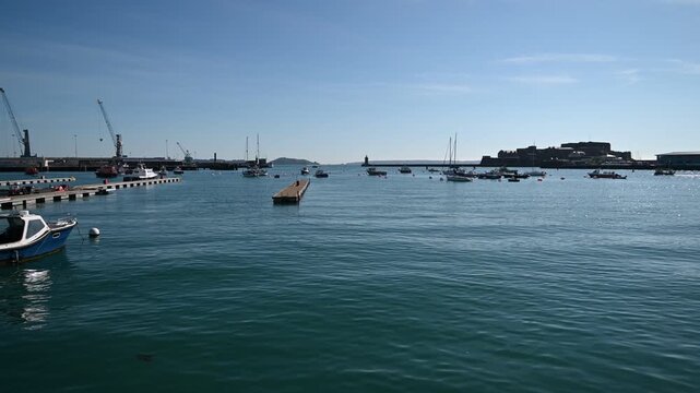 St Peter Port Harbour,Guernsey Channel Islands.Water level view of boat bobbing in the harbour looking towards docks and Castle Cornet with Jethou visible through harbour entrance in afternoon sun