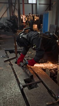 Vertical shot of professional metalworker in protective helmet using angle grinder on steel bar, creating bright sparks. Footage is suitable for industrial safety and manufacturing ads