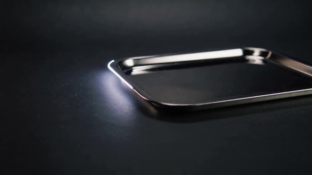 Shifting linear light and minor pan moving across steel tray on dark tabletop, highlighting rim