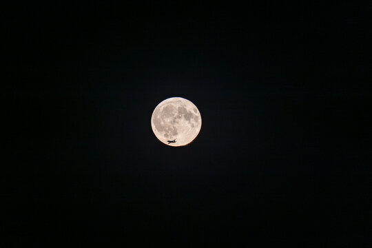 View of a silhouette of an airplane flying across the bright full moon in the night sky in Berlin, Berlin, Germany.