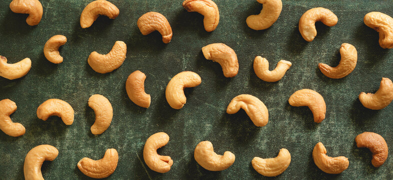 Roasted cashew nuts on textured rustic green highlighting their curved shapes and warm golden tones.
