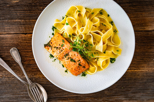 Pasta with baked salmon steak on wooden table
