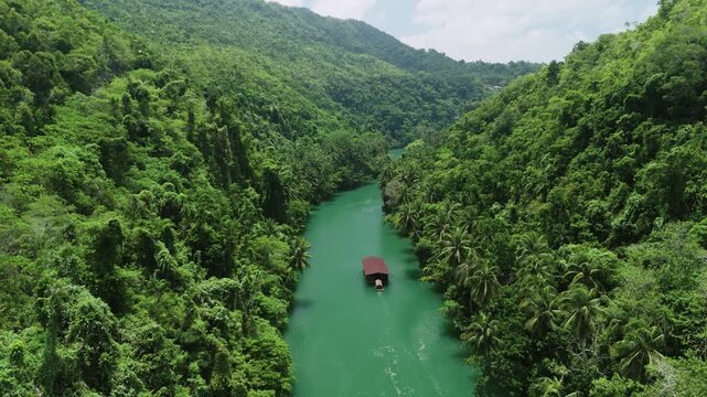 Aerial view of the Loboc River Cruise boat navigating the lush green river surrounded by dense tropical jungle in Loboc, Central Visayas, Philippines.